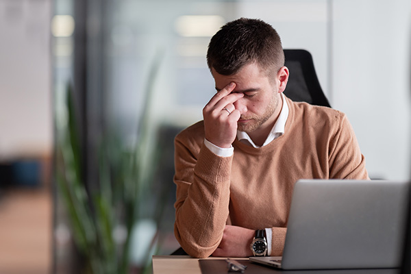 Businessman experiencing headache, fatigue, burnout, and stress in the office while working on a laptop.