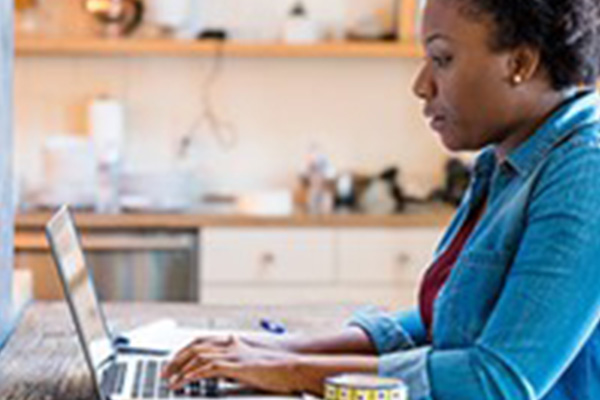 Adult student studying on a laptop at home while taking notes for long-term learning.