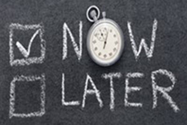 Chalkboard with 'NOW' in a checked box and 'LATER', with a stopwatch for the 'O' in NOW, symbolizing the importance of acting immediately.